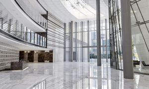 Modern glass atrium with marble floors, tall metal columns, and escalators in a bright office lobby